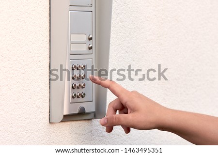 The hand of a young woman enters a numeric code on the keypad of an electronic lock or doorbell. Royalty-Free Stock Photo #1463495351