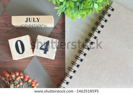 July 4. Date of July month. Number Cube with a flower and notebook on Diamond wood table for the background.
