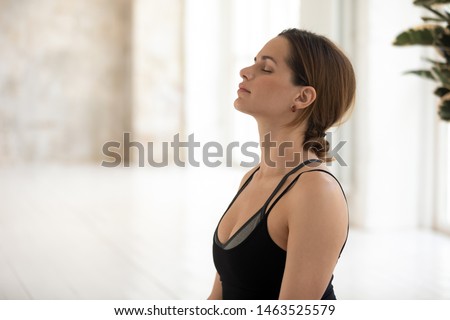 Young serene woman wear sportswear closed eyes meditating indoors, starts day with yoga workout feels placid, no stress reduces anxiety filling with positive energy, inner harmony healthy life concept Royalty-Free Stock Photo #1463525579