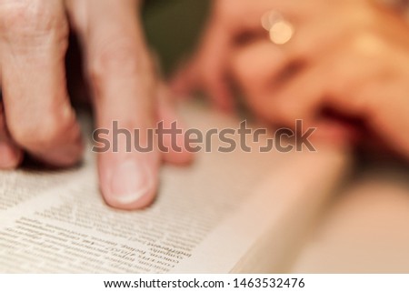 Selective focus of word in book with the hand pointing out for searching word.
Reading the book with index finger leading may increased speed of reading.