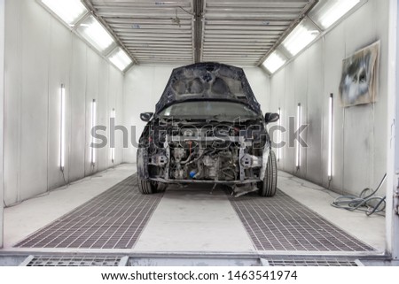 The black car after a serious accident with a completely broken front of the body with open hood that is awaiting repair in a room of workshop for body paint of vehicles. Auto service industry