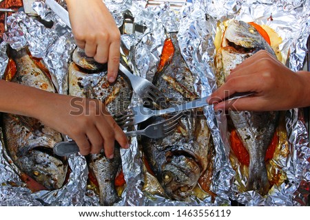 four baked dorado fish in foil with vegetables for a family holiday dinner, children's hands with forks prick a fish