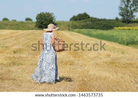 Mature woman in a wheat field in a warm summer day. Old Woman with wicker basket. Woman with wicked basket full of flowers. Warm summer day. Country. 