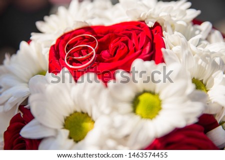 Wedding rings are on the bride's bouquet, Wedding bouquet of white daisies and red roses. Wedding background for cards and invitations.