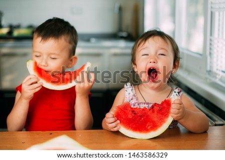 Children, brother and sister, boy and girl in the kitchen eating watermelon, very fun and cute