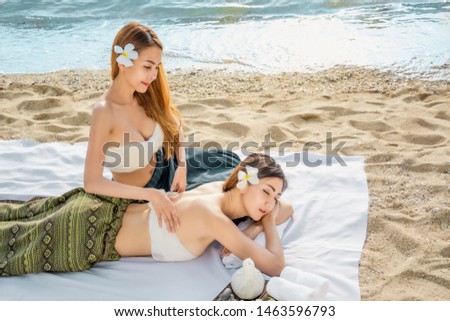 Masseuse doing massage and spa for young beautiful asian women who are sleeping on white cloth on sand beach, with concept of charging life energy and relaxing body for a refreshing holiday