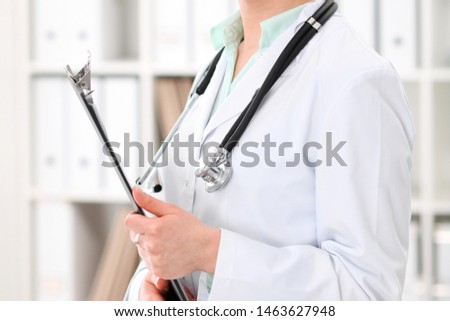 Stethoscope at female doctor breast at hospital office. Unknown physician's hands close-up. Green tone of blouse. Medicine and health care concept