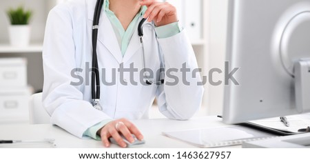 Doctor woman sitting at the desk with computer at workplace in hospital office. Unknown physician's hands close-up. Green tone of blouse. Medicine and health care concept