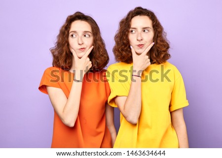 serious puzzled young twonsisters holds both palms on chin looks away, aside.isolated over blue background. studio shot, It's a great idea, plan for business