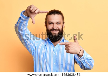 happy positive handsome young man making frame with fingers isolated on a yellow background. camera. man is pretending that he is taking a photo