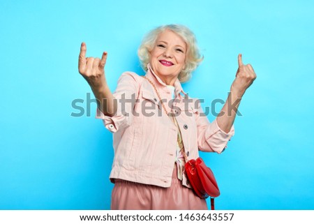 elder cheerful positive gorgeous lady making rock sign, isolated blue background, studio shot. body language, lifestyle, free time, spare time