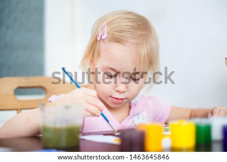 Cute little blonde girl painting a picture in home studio
