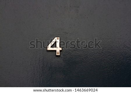 House number four with the 4 in metal on a black wooden front door