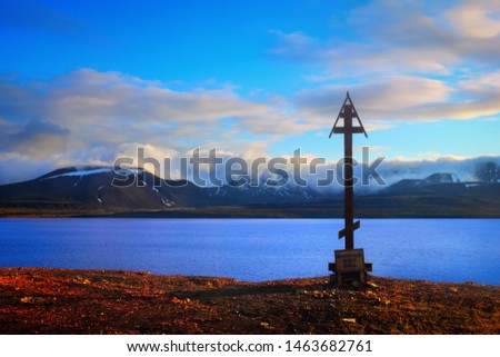 Old wooden cross with inscription: "Pomor sign cross of the 18th century ad", at the background of dark rocks, blue evening sky and sea water in Barentsburg, Svalbard and Jan Mayen, Norway, Europe