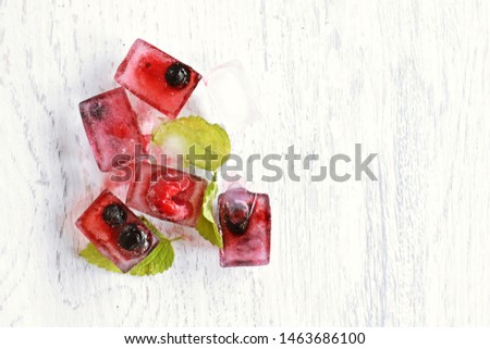 Ice cubes with various berries freezing inside lie on a light wooden surface, as refreshing cooling in the summer - Delicious and organic berries in ice cubes