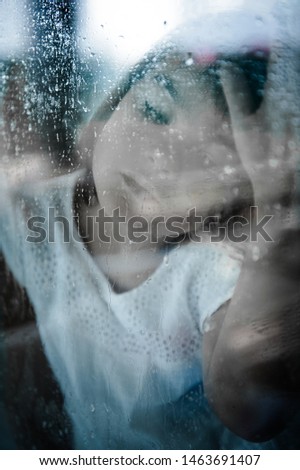 European appearance girl is sitting at the window, sad, on the window raindrops