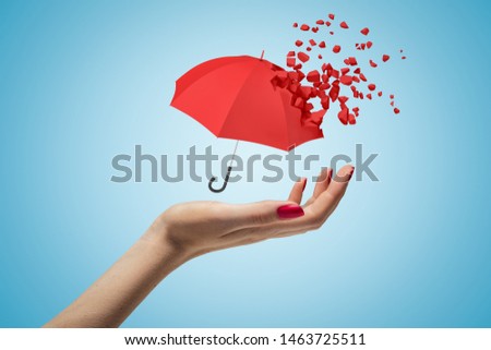 Closeup of woman's hand facing up and levitating small red umbrella that has already started dissolving into pieces on light blue background. Weather and climate. Climate change. Weather modification.
