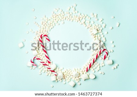 Christmas layout with candy cane and different sizes marshmallows on a turquoise background in the form of a circle shape. Concept for new year postcard with space for text.