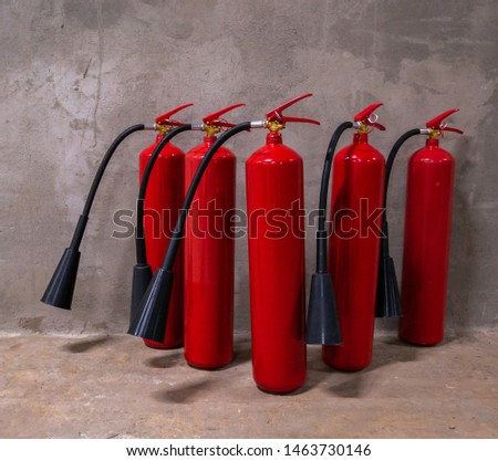 Row of five red fire extinguishers in a shop against gray concrete wall