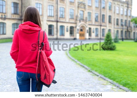 Behind view photo portrait of nervous scared stressed teen person looking at the door of her new place of studying wearing bright clothes standing near green lawn