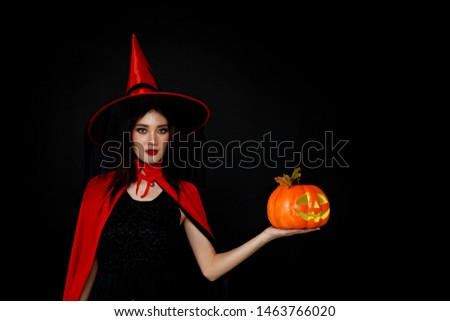 Woman in witches hat with carved halloween pumpkin in Halloween theme on black background.                              