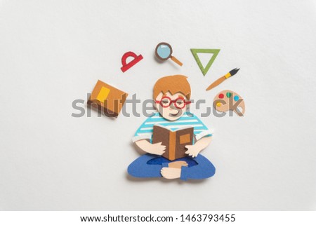 Boy in glasses sitting in lotus pose and reading educational textbook. Book, protractor, magnifier, triangle ruler palette of watercolors, paint brush around schoolchild. Back to school concept