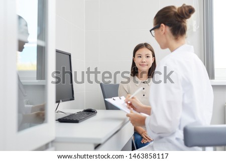 Portrait of little Asian girl listening to female doctor during consultation, copy space