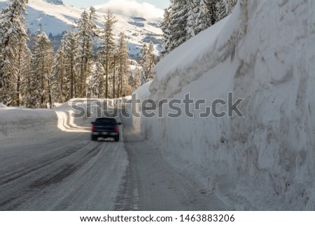 Unidentified moving vehicle on mountain road highway 88 towards Carson Pass, California, USA, on a winters day featuring five feet of snow on the side of the road after several storms.