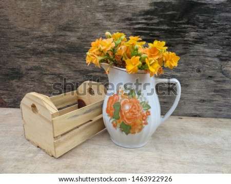 Bouquet of small yellow flowers (Kalanchoe) in vintage porcelain milkmaid, mini wooden box beside. Aged wood background. Rustic decor composition with copy space.                               