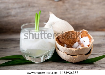 Fresh coconut juice in a glass with coconut white meat and peeled coconut on wood background.