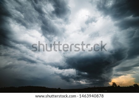 Dramatic cloudscape. Sunny light through dark heavy thunderstorm clouds before rain. Overcast rainy bad weather. Storm warning. Natural gray background of cumulonimbus. Sunlight in stormy cloudy sky.