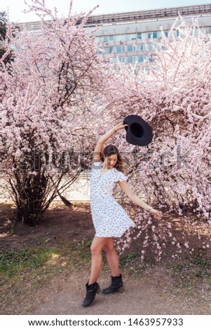 Charming beautiful lady with a lot of positive emotions with sakura tree through blooming time, in black hot and shoes