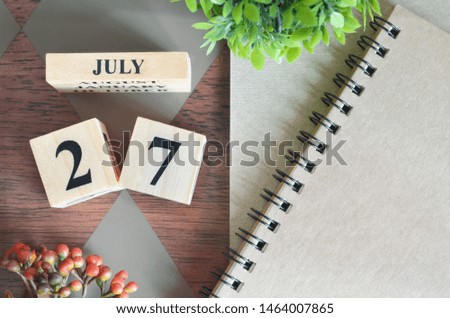 July 27. Date of July month. Number Cube with a flower and notebook on Diamond wood table for the 