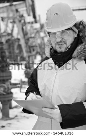 Engineer in uniform and helmet on of background the pump jack. Black and white.
