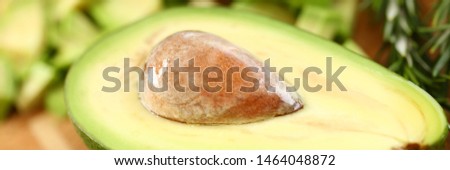 Tropical Avocado Fruit Half Holding Brown Seed. Exotic Ingredient on Wooden Cutting Board. Dieting and Healthy Food with Rosemary Herb. Tasty Appetizer. Partial View Horizontal Photography