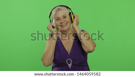 An elderly woman listens to music in headphones. Old pretty grandmother in a purple dress. Place for your logo or text. 