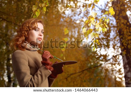 Young beautiful woman posing with palette and brush outdoors in autumn park.