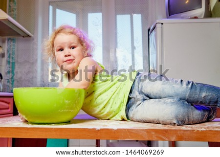 Emotional Small girl with big green plate in the kitchen on the table