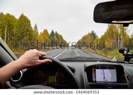 Track from the car window. Woman's hand on the steering wheel. Female driver seeing autumn landscape during travel in auto
