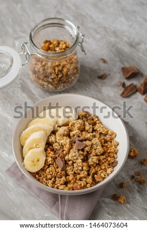 Breakfast with granola with banana. Pieces of chocolate and jar of granola on background.Stock image