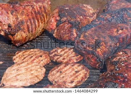 Beef brisket and hamburgers cooking side by side on an open bbq grill. traditional street fair food.
