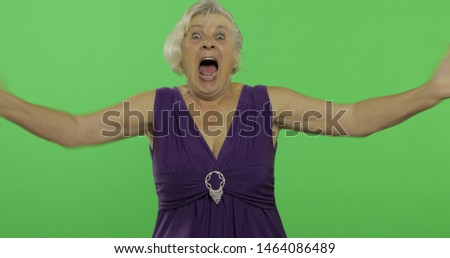 An elderly woman shows amazement, joy and smiles. Old pretty happy grandmother in a purple dress. Place for your logo or text.