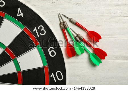 Dart board with color arrows on white wooden background, top view