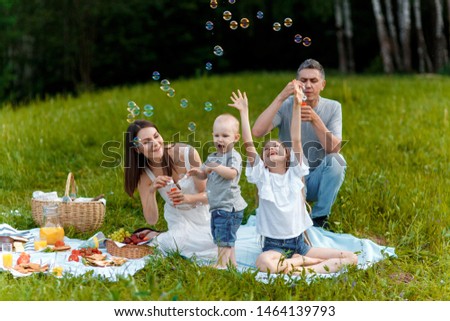 young family on the nature in the forest at a picnic. mom dad son and daughter are resting in nature. children catch soap bubbles.