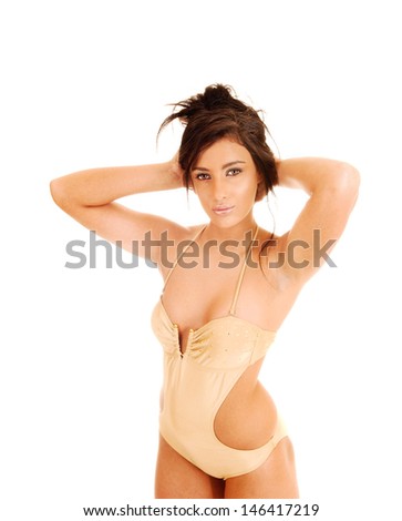 A closeup picture of a lovely teen girl standing for white background in a gold color bikini with her hands behind her head. 