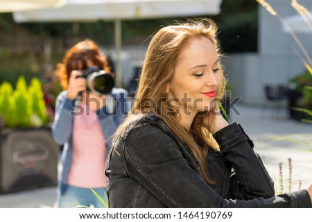 Happy woman having portrait photo shoot. Young adult female and photographer taking pictures in background.