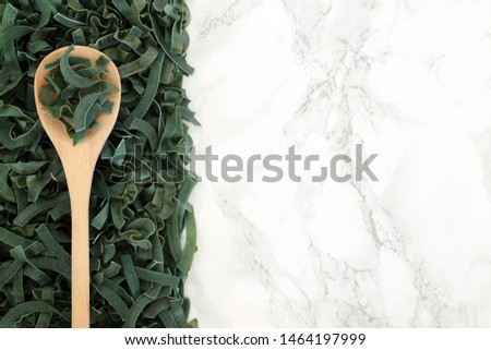 Spirulina tagliatelle health food pasta on an olive spoon and loose forming an abstract background on marble with copy space. High in protein and dietary fibre.