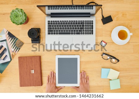 Close-up of businesswoman sitting at wooden table with laptop notepad and holding digital tablet with blank touchscreen while drinking tea