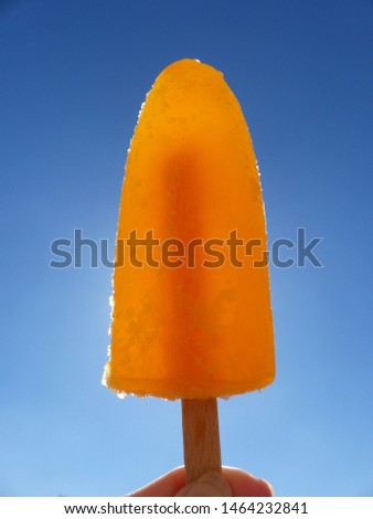 Frosted orange ice Popsicle held up to the sun. 