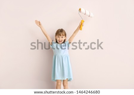 Little girl with paint roller near light wall